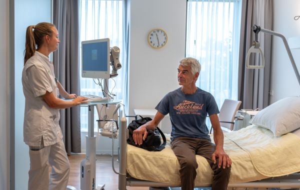 Verpleegkundige achter monitor spreekt met patiënt