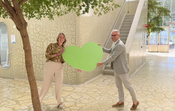 Bestuurder Mario Korte en programmamanager duurzaamheid Anoek van Doorenmaal houden een groen hart vast in het hal van het Maxima MC