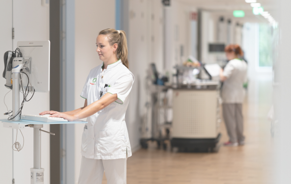 Verpleegkundige in ziekenhuisgang aan het werk op een laptop