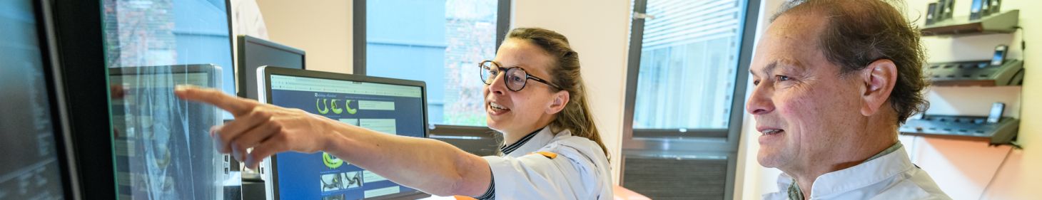 Artsen bespreken uitslag van patiënt met elkaar aan bureau. Op het bureau staan verschillende schermen, waarop de gegevens te zien zijn.   