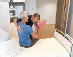 Patiënt wordt uit bed geholpen door familielid of bekende